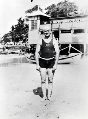 Member of Manly Surf Club, Stewart Wright of the 'A' team, with Manly Surf Club pavillion in the background