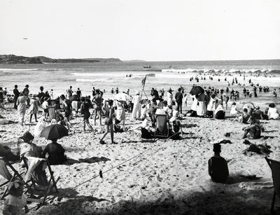 Manly Beach showing a large number of people bathing and sitting on the sand, with a surf boat beyond the breakers