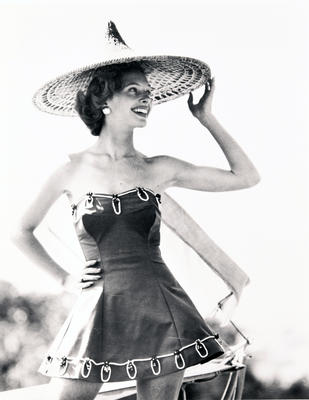 Female wearing 'sports de jour fashion' strapless costume, skirt, white piping at top and bottom, straw hat