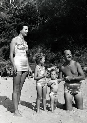 Female wearing 'sports de jour fashion' man, woman and two childresn in satin-look bathing suits.