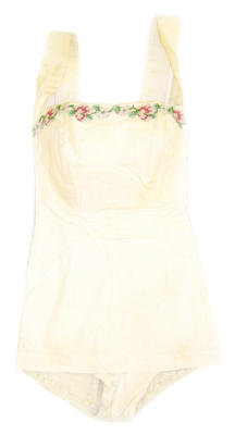 Cotton white with e pink green and purple flowers across top, attached with silver thread, vertical seams down front shirring across back skirt front facing tie behind neck machine sewn