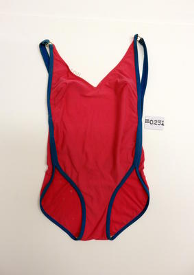 Hot pink swimsuit in polyester/cotton/lycra with blue elasticised trim in continuous band from outer shoulder to around the leg, joined with gold metal ring at shoulder. It has a "v" neck at front and plunging back.