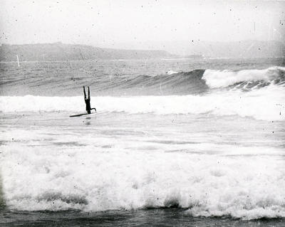 Man doing a headstand on a surfboard while riding a wave