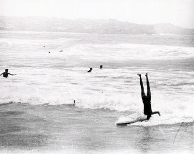 Man doing a headstand on a surfboard while riding a wave