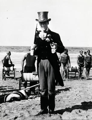 Man in a top hat on Manly Beach during a surf carnival