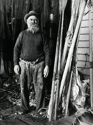 Unidentified elderly man surrounded by boating paraphernalia (nets, oars, rope etc)