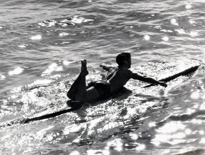 Man on long board paddling in the sea.