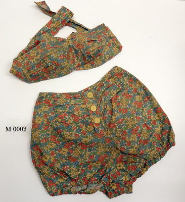 Halter neck, orange yellow green and blue floral fabric, bloomers have three buttons down front.