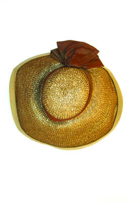 Straw hat khaki with grosgrain ribbon trim on rim of wide brim green bronze fabric pleated and tied around low flat crown brim narrower at rear black elastic chine strap hand made machine sewn