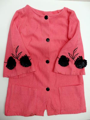 Beach coat, pink terry towelling with black embroided floral design on sleeves, black raffia flowers, black buttons, two pockets on front. 3/3 sleeves