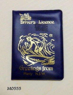 Blue plastic driver's license holder with gold stencilled surfer print on front rectangular shape opens with two clear plastic pockets inside machine made