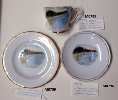 Teacup bone china white with colour transfer print of Manly Beach showing beach many bathers pine trees label 'Surfing beach Manly NSW' gold paint on inner rim and decorating handle