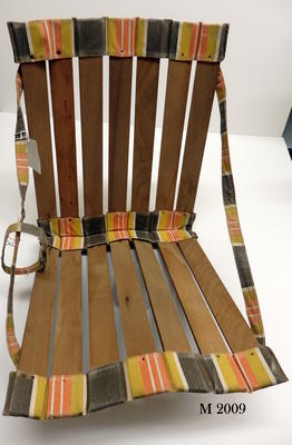 Fold-up beach chair. Wooden slats canvas straps. canvas edges nailed striped orange, black, white & mustard canvas colours. Rolls-up secured by canvas strap, strap handles to carry.