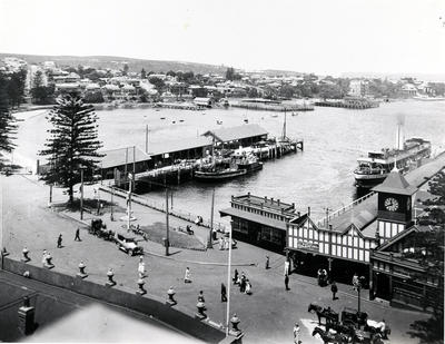 Over Manly Wharf area, showing passenger wharf, cargo wharf and forecourt, with Manly Baths, Sailing Club? and other structures along the eastern shore and on the Eastern Hill.