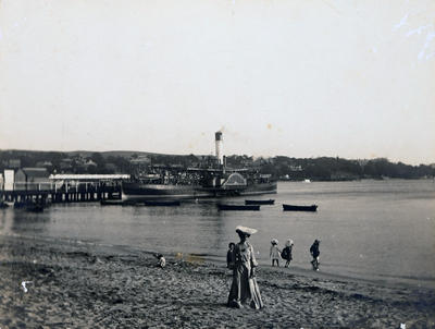 Wharf and part of beach west of the wharf alongside the wharf is a double-ended paddle-steamer. In the foreground is Mrs M Condon, grandmother of donor. Eastern shore in background