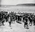 Crowd surrounding 'Duke' Kahanamoku as he carries his surfboard up the beach